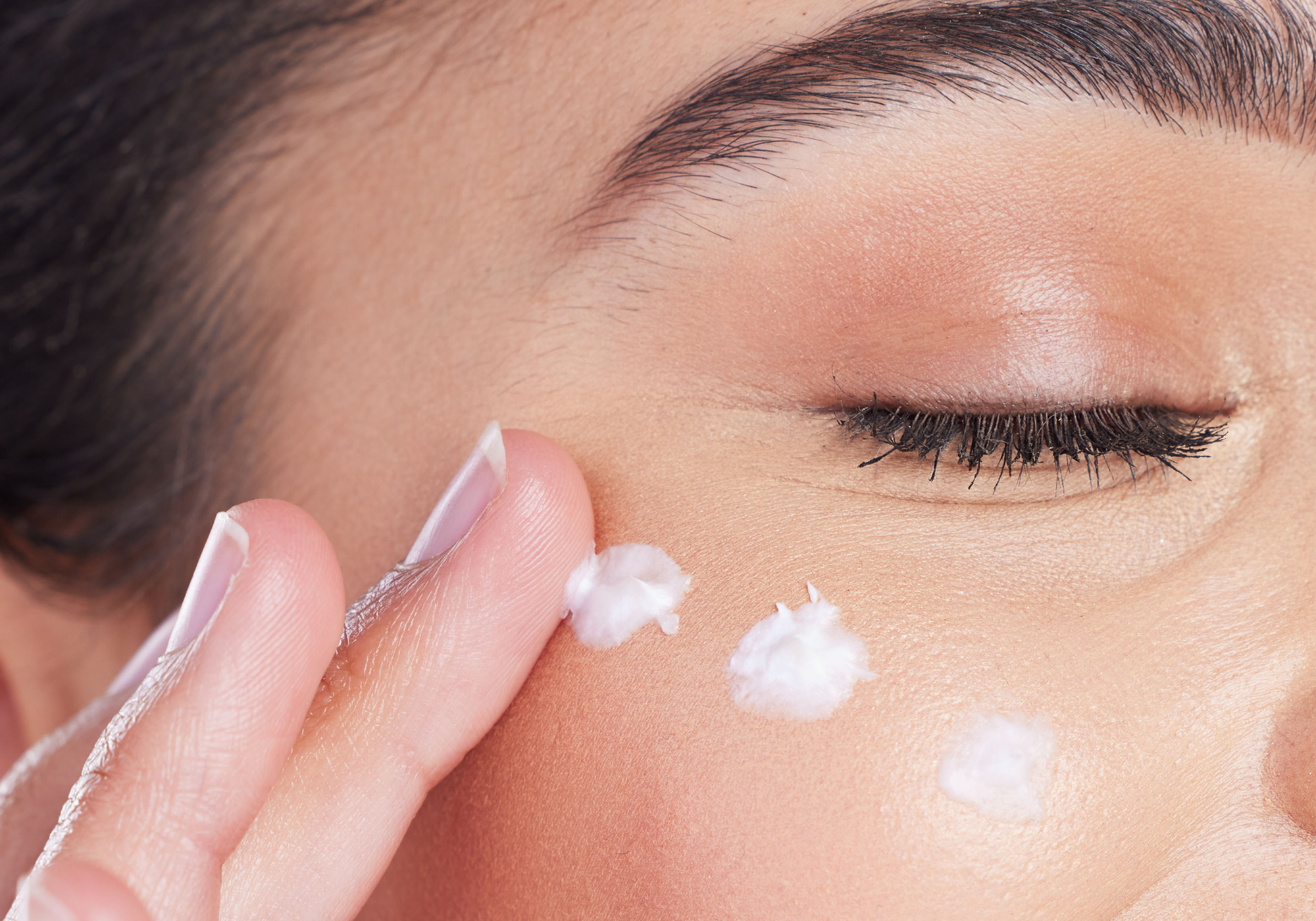 Close up of woman applying three dots of cream onto her undereye area